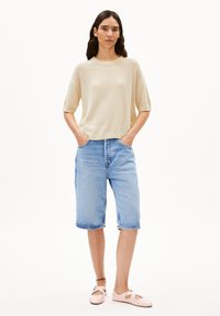 Beige gerippter kurzärmliger Pullover, hellblaue knielange Jeansshorts und blassrosa flache Schuhe mit Riemen. Einfaches Design, lässige Passform.