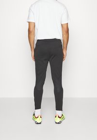 Svarta sportbyxor med en åtsittande passform, med paneldetaljer och dragkedjor vid vristerna. I kombination med vita strumpor och färgglada träningsskor.