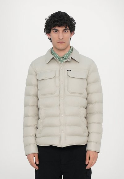 Chaquetón acolchado de color beige claro con cierre de botones en la parte delantera, dos bolsillos en el pecho y bolsillos laterales. Presenta un cuello clásico y textura de nailon.