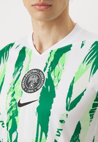 Maillot de football blanc avec des motifs abstraits verts et vert clair. Présente un emblème rond et un logo Nike noir sur la poitrine.