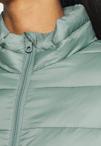 Giacca puffer verde menta con colletto alto, dotata di zip a tutta lunghezza e motivo a righe orizzontali per l'isolamento. Texture liscia e lucida.