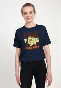 Námořnické tričko s grafickým designem, který obsahuje světle žluté 3D kostky a text "MINECRAFT" v oranžové a hnědé barvě, vyrobené z bavlněné tkaniny.