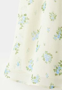 Tissu crème avec de délicats motifs floraux bleus et des feuilles vertes réparties uniformément sur le matériau.