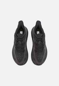 Scarpe da ginnastica nere con una parte superiore testurizzata, caratterizzate da un motivo geometrico. Suole arrotondate con lacci e un logo circolare sulla linguetta.