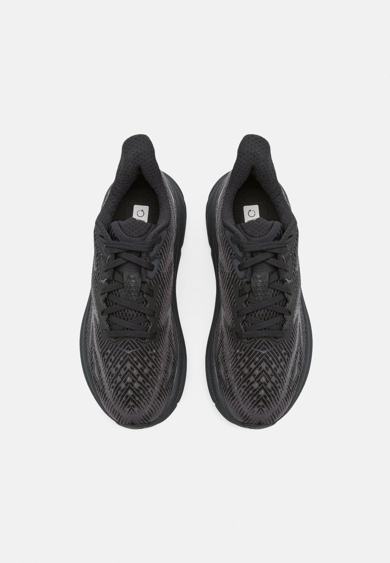 Schwarze Sportschuhe mit einer strukturierten Oberfläche, die ein geometrisches Muster aufweisen. Abgerundete Sohlen mit Schnürsenkeln und einem runden Logo auf der Zunge.