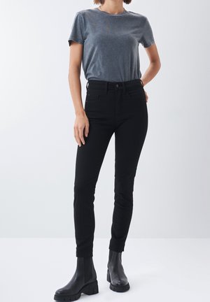Jeans negros ajustados con una cintura alta, con una textura suave y diseño de cinco bolsillos. Combinados con una camiseta gris de cuello redondo y botas negras.