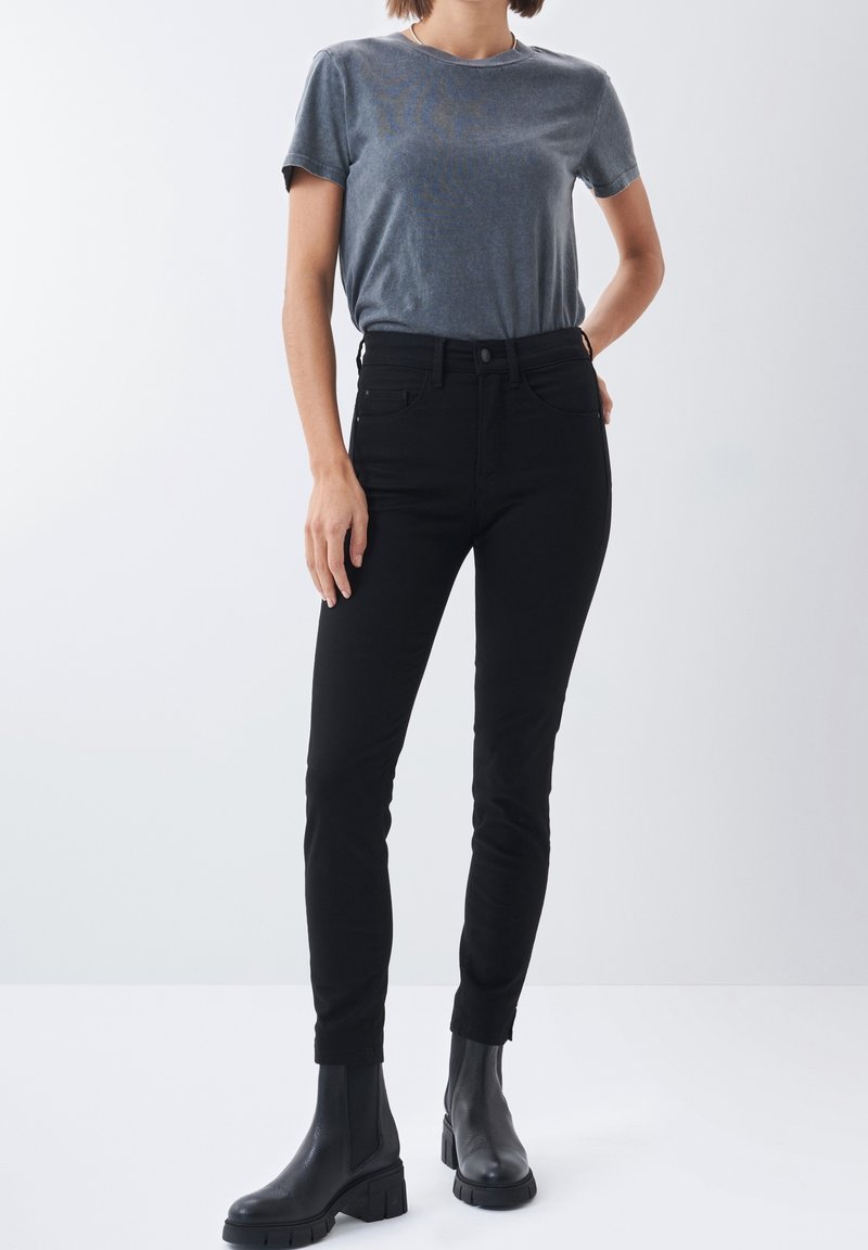 Jeans negros ajustados con una cintura alta, con una textura suave y diseño de cinco bolsillos. Combinados con una camiseta gris de cuello redondo y botas negras.