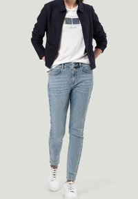 Navy jacket with a round collar over a white graphic t-shirt, paired with light blue skinny jeans and white sneakers.