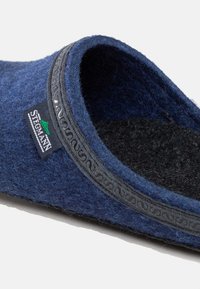 Navy blue felt slipper with a textured surface, black inner lining, and a decorative black trim. Features a logo tag on the side.