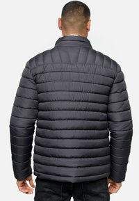 Chaqueta acolchada gris con costuras horizontales, cuello alto y mangas largas. Presenta una textura suave y brillante con un corte regular.