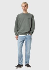 Grå sweatshirt med ribbade mudd, med en liten svart logotyp på bröstet. Pairad med ljusblå jeans och svarta sneakers.