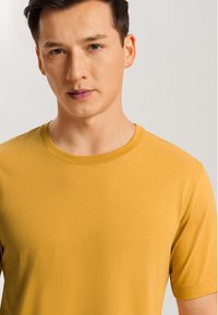 Kortärmad T-shirt i senapsgul, tillverkad av mjukt och slätt tyg. Har en klassisk rund halsringning och en avslappnad passform.