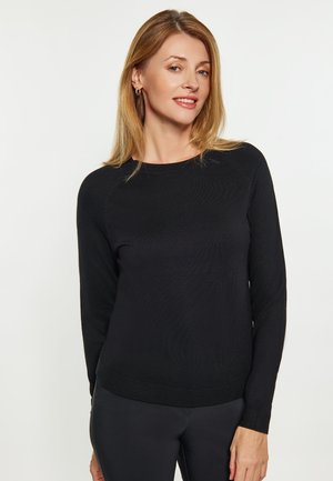 Black long-sleeve sweater with a ribbed neckline, textured fabric, and fitted design. Worn with black pants, featuring a soft, smooth finish.