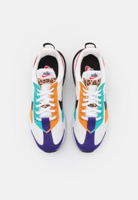 Paire de baskets Nike avec base blanche, bouts violets, panneaux turquoise et orange, languettes imprimé léopard, et lacets blancs sur fond blanc.
