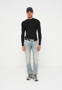 Schwarzes Langarmshirt, hellblaue Jeans mit Used-Effekten und schwarze Sneakers mit weißen Details. Modell trägt eine graue Mütze und einen schwarzen Gürtel.