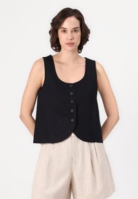 Colete preto sem mangas com decote redondo e fecho de cinco botões, apresentando um design ajustado e uma bainha curva. Usado sobre calções de cor clara.