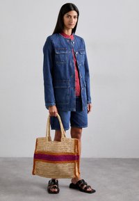 Traper jakna s četiri prednja džepa, nošena preko crvene majice i traper kratkih hlača. Bež slamnata torba s šarenim horizontalnim prugama. Crne sandale.