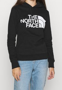 Svart hoodie i bomull med en känguruficka, med en stor vit grafisk logotyp på framsidan. Elastiska manschetter och nederkant.