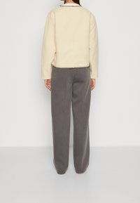 Kremowa, krótka kurtka z okrągłym dekoltem i kontrastującymi, ciemnymi przeszyciami. Szare, wysokogatunkowe spodnie o szerokich nogawkach z gładką teksturą.