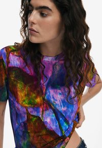 T-shirt a maniche corte multicolore con un vivace motivo astratto in tonalità di blu, viola, verde e rosso. Realizzato in tessuto leggero.