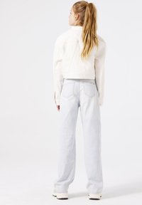 Chaqueta de mezclilla blanca, cortada, combinada con pantalones de mezclilla anchos de color azul claro. Incluye un ajuste entallado, bolsillos traseros y una textura suave.