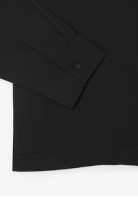 Poignet de chemise noire à manches longues avec un bouton et une texture subtile à motif quadrillé sur le tissu.