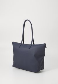 Sac fourre-tout bleu marine avec une texture lisse, deux longues poignées et une fermeture éclair. Il présente un design minimaliste et une forme structurée.