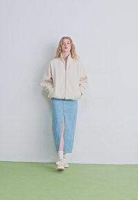 Fleece jakna na zadrgo v svetlo bež barvi, v kombinaciji s kratko denim krilo v modri barvi, ki ima sprednji razporek. Obleko dopolnjujejo bele superge.