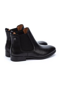 Botas de tobillo de cuero negro con paneles elásticos en los laterales, punta redondeada y un diseño minimalista. Presenta un pequeño acento metálico en la parte trasera.