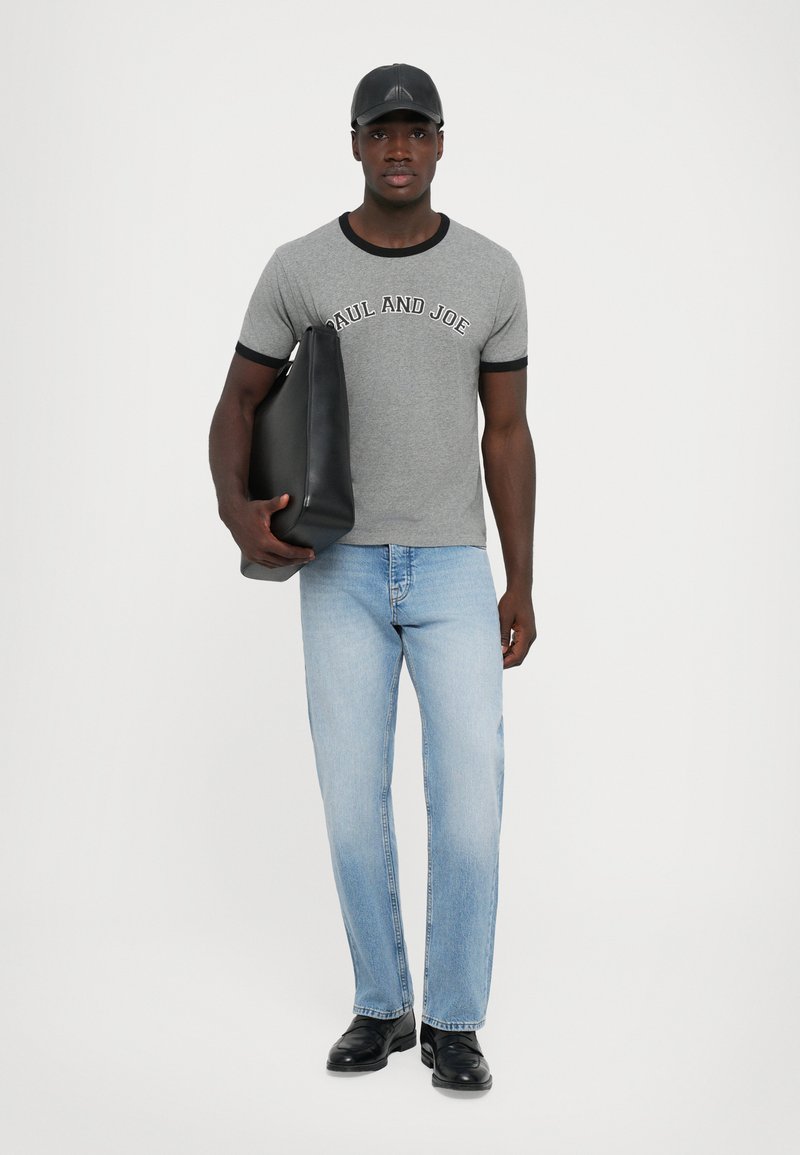 Gray t-shirt with black trim featuring "PAUL AND JOE" text, light blue straight-leg jeans, and black shoes, holding a black tote bag.