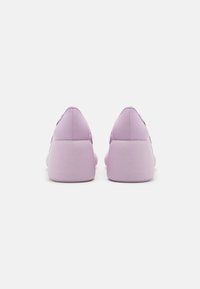 Lila sneakers med en texturerad gummisula, som har en slät syntetisk ovandel och en låg profil-design. Bakifrån kan man se sömnadsdetaljer.