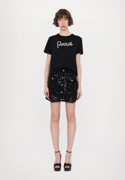 Svart t-shirt med "Paris" i rhinstenar, matchad med en svart mini kjol i paljetter som har framfickor och dekorativa knappar. Svarta plattformssandaler.