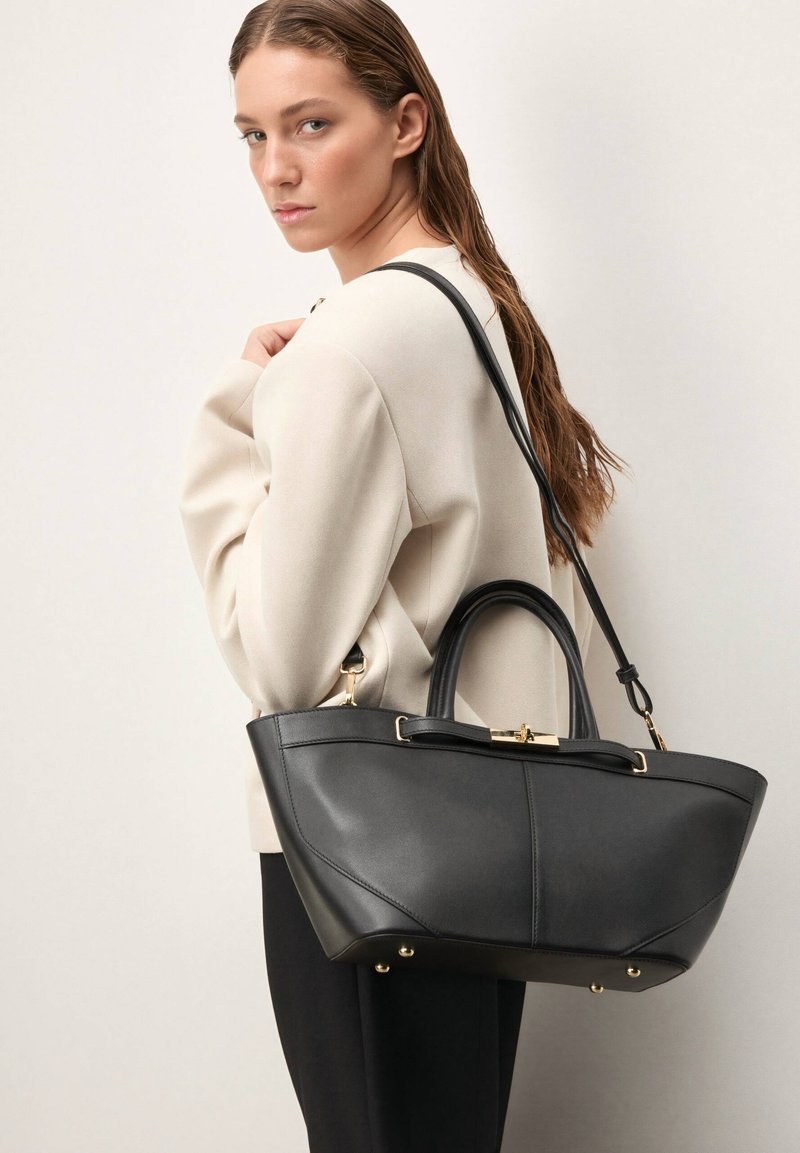 Juoda odinė rankinė su struktūruota forma, dviem rankenomis ir nuimamu peties dirželiu. Papuošta auksiniais metaliniais akcentais.
