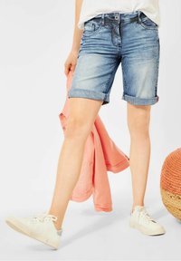 Dżinsowe szorty w paski, z zagiętymi mankietami i jasnoniebieskim odcieniem. Połączone z białymi sneakersami i różową kurtką.