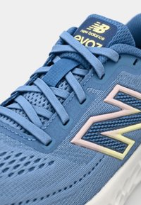 Scarpa sportiva blu con tomaia in knit testurizzato, logo New Balance in evidenza in rosa e giallo, e lacci piatti. Suola in schiuma leggera.