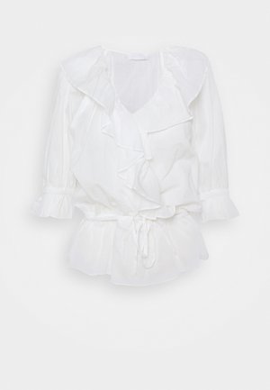 Blouse blanche à manches longues avec col en V à volants, devant croisé, ceinture à nouer et poignets et ourlet à volants.