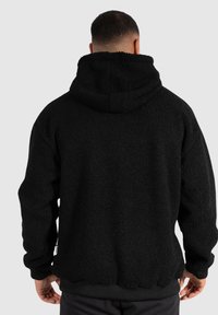 Svart fleecehoodie med en mjuk, strukturäd yta, stor luva och elastiska ärm- och nederkanter. Har en avslappnad passform och ingen synlig logotyp.