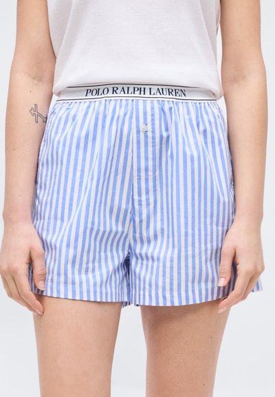 Κοντινό πλάνο προσώπου που φοράει μπλε και άσπρα κάθετα ριγέ σορτς με άσπρη ζώνη μέσης με επιγραφή "Polo Ralph Lauren" και λευκό αμάνικο τοπ.