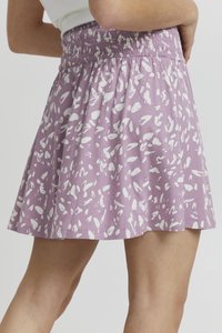 Lyslilla nederdel lavet af blødt stof, med et hvidt abstrakt mønster, smocket talje og en flagrende design.