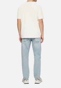 Witte katoen t-shirt, ontspannen fit, korte mouwen. Lichtblauwe jeans met een vervaagde was, recht model. Grijze sneakers met subtiele details.