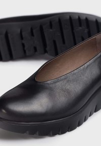 Zapatos de cuero negros con punta redonda, corte bajo y suela gruesa y texturizada negra que presenta surcos para tracción. Superficie suave.