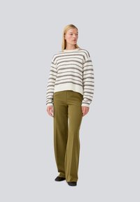 Maglione a righe in crema e marrone, abbinato a pantaloni ampi verde oliva, con una vestibilità comoda e maniche lunghe. Calzature nere.