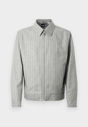 Sivá bunda na zips s vertikálnymi pruhmi, vyrobená z textúrovaného materiálu. Má špicatý golier a dlhé rukávy. Jednoduchý, moderný dizajn.