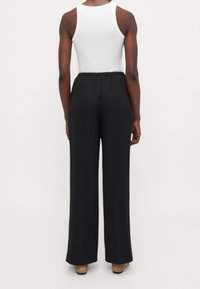 Mustat leveälahkeiset housut, joissa on rento istuvuus, elastinen vyötärö ja sileä kangas, yhdistettynä valkoiseen hihattomaan paitaan.