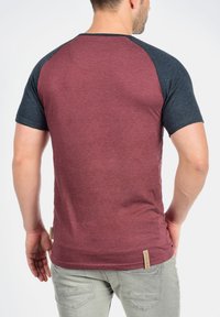 Maroon T-shirt with dark blue raglan sleeves. Made of soft fabric, features a rounded neckline and a small logo tag on the lower side.