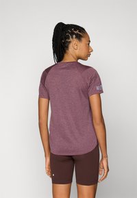 Camiseta atlética de mangas curtas em tecido borgonha mesclado, com mangas raglan e uma bainha curva. Acompanhada de calções castanhos com detalhe de logótipo.