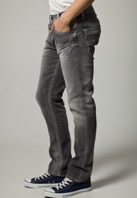 Grå denimjeans med slim fit, med en subtil blekning, femficksdesign och slitna detaljer. Kombineras med marinblå sneakers.