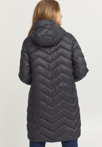 Polstret mørkegrå frakke med et zigzag mønster, en hætte og lange ærmer, der har en let skrædderlignende design og en mellem-længde.
