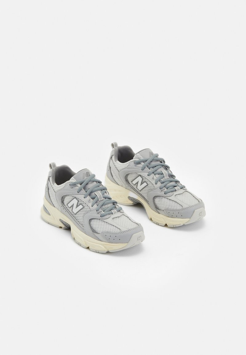 Paire de chaussures de course New Balance grises et blanches avec tissu en mesh et semelles épaisses beige sur fond blanc.