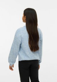 Šviesiai mėlynas, purvus megztinis su apvaliu kaklu ir pūstomis rankovėmis, derinamas su juodomis kelnėmis, matomas iš nugaros.